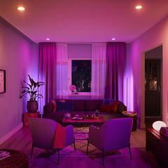 Living room with purple lighting, sofa, chairs, and decorative items.