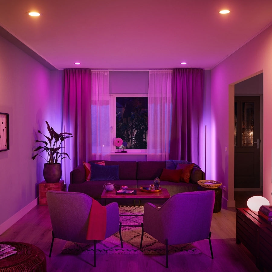 Living room with purple lighting, sofa, chairs, and decorative items.